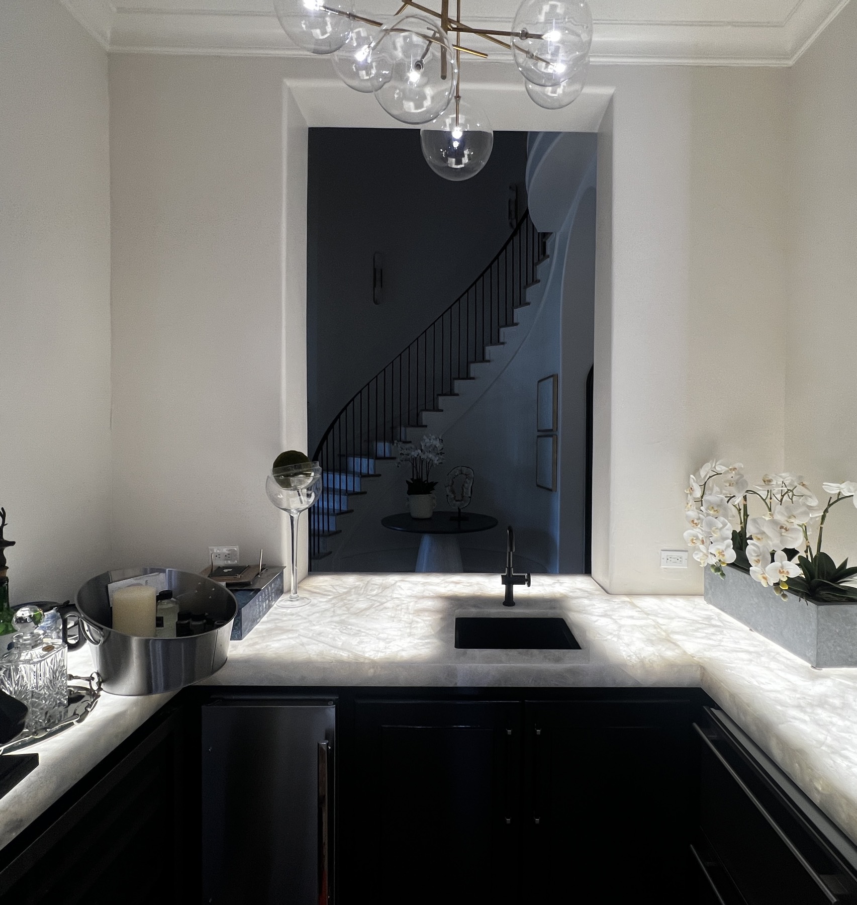 Wet bar with fully illuminated stone countertops beside a curved staircase